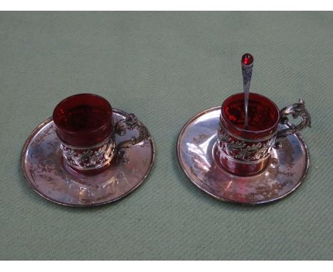 TWO SILVER COLOURED AND CRANBERRY GLASS COFFEE CANS, WITH SAUCERS AND SPOONS 