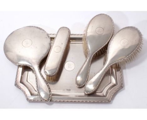 1920s silver dressing table set comprising three hair brushes and a hand mirror with engine turned decoration, together with 