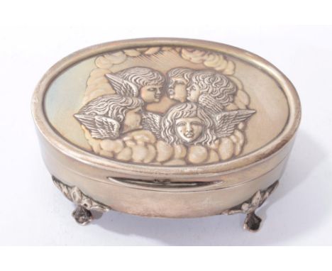 Edwardian silver trinket box of oval form with hinged cover embossed with angel faces and velvet interior, on four decorative