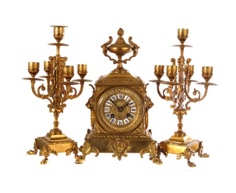 A gilt clock garniture with fine branch candelabras, the gilt clock face with black Roman numerals on white enamel panels, su