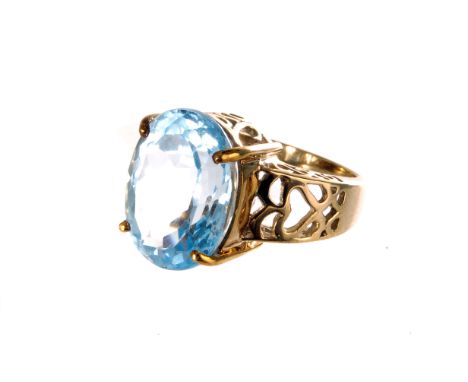 A 9ct gold and blue topaz dress ring, the oval cut stone in high single claw mount, with pierced design to the shoulders, siz