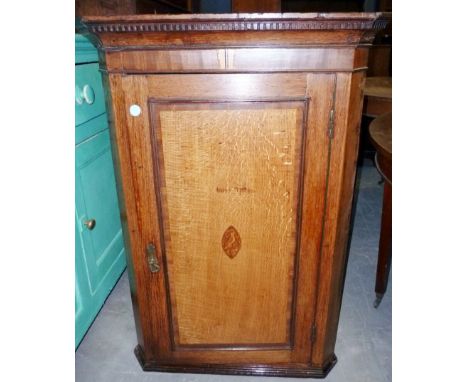 A late Georgian oak corner cupboard, the dentil cornice surmounting a shell paterae decorated panel door enclosing drawers an