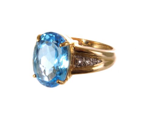 A 9ct gold and blue topaz dress ring, the large oval cut stone set in single claw mount, flanked by two small clear stones to