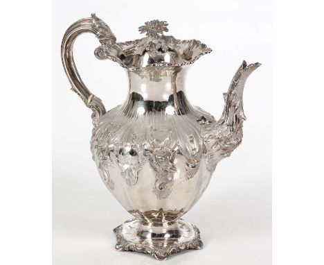 The hinged cover applied with a floral finial, wavy rim, the body embossed with scrolls and flowers, leaf-capped handle, rais