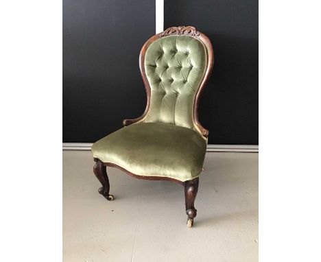 Victorian mahogany buttoned back easy chair upholstered in green material with carved front legs on brass and ceramic casters
