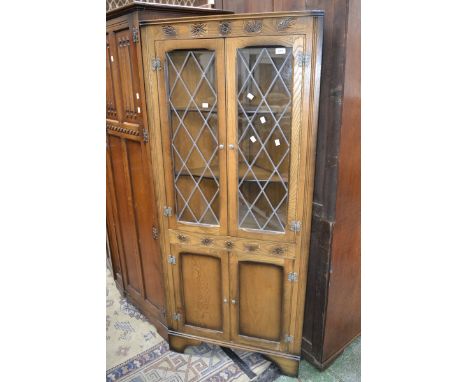 A floor standing corner cupboard, lead glazed doors to top carved panel doors to base.