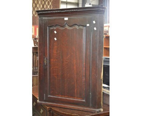 A George III oak wall mounted corner cupboard, stepped cornice, canted angles, panel door