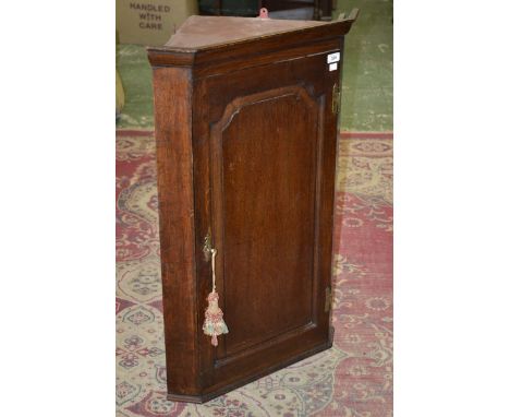 A George III wall mounted oak corner cabinet of small proportions, outswept cornice, canted angles, crossbanded panel door. 9