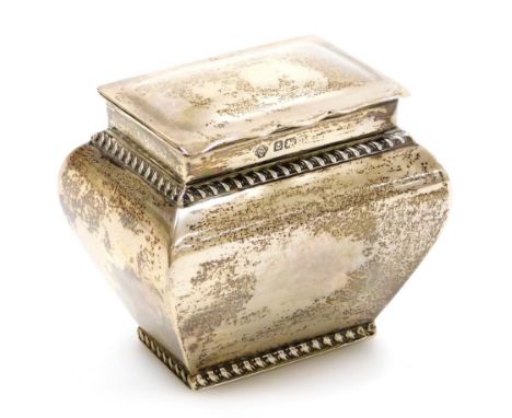 A George V silver caddy, with a shaped top, gadrooned borders and plain tapering body, the hinged lid enclosing a vacant inte