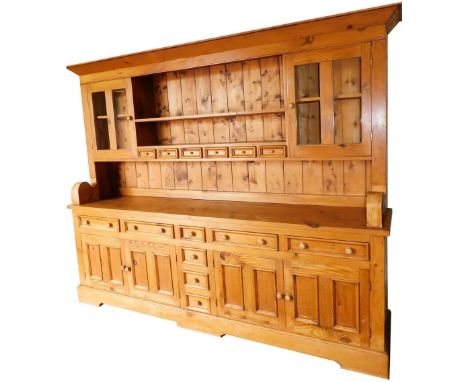 A pine dresser, the out swept pediment over a two shelf Delft rack and six spice drawers, flanked by two glazed doors enclosi