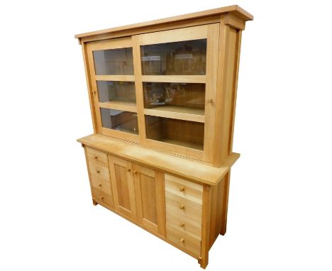 A light oak dresser, the pediment over a pair of glazed sliding doors, enclosing four shelves, above a pair of cupboard doors