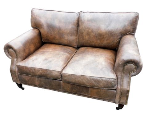 A brown leather two seater sofa, with brass studded outline, raised on four block feet terminating in brass castors, 153cm wi