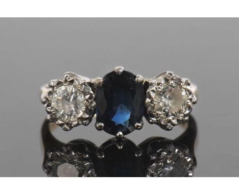 Sapphire and diamond three stone ring centering a dark oval shaped faceted sapphire flanked by two round brilliant cut diamon