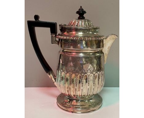A late Victorian silver embossed hot water jug with ebonised finial and handle, raised on a circular base (by Charles Stuart 