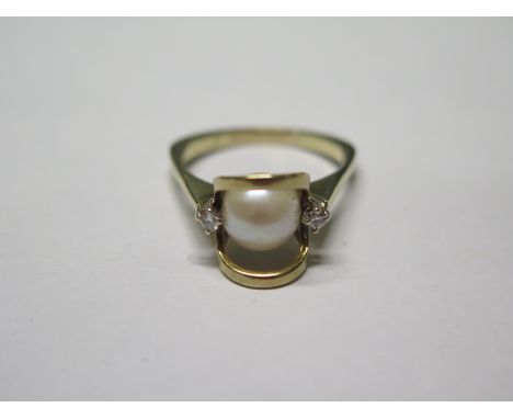 A 14ct yellow gold pearl and diamond ring in a modern setting set with two small brilliant cut diamonds flanking a large cult