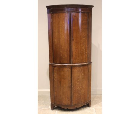 A George III oak and mahogany crossbanded freestanding bowfront corner cupboard, inlaid with stringing, the moulded cornice o