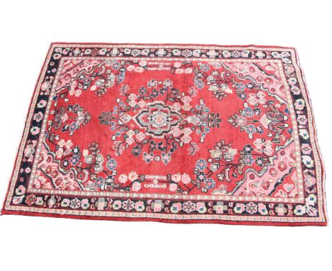 A washed red ground hand woven Persian Sarouk village rug, centred with a floral medallion, 196cm x 130cm