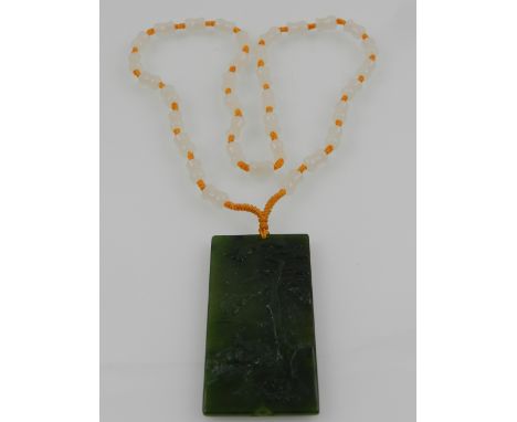 A Chinese spinach jade pendant of rectangular form, decorated with a heron beneath trees, suspended on a white jade beaded ne