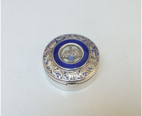 A CIRCULAR LIDDED SNUFF WITH ENAMEL DECORATION, the white metal body with scrolling band to hinged lid and central basket of 