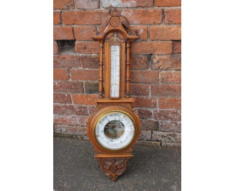 A LATE 19TH/ EARLY 20TH CENTURY CARVED OAK ANEROID BAROMETER, the unusual enamel dial with visible mechanism, the dial named 