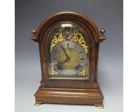 A WINTERHALDER & HOFMEIER OAK CASED MANTEL CLOCK, the arched case having brass finials and raised on four brass bracket feet,