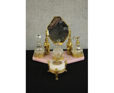 An Art Deco Egyptian Revival pink marble and gilt metal dressing table set complete with glass scent bottles, atomisers and a