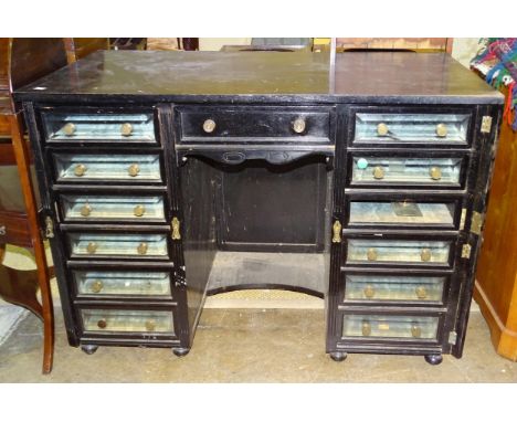 An unusual Edwardian ebonised kneehole cabinet of drawers, the central drawer flanked by twelve glass-fronted baize-lined dra