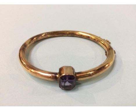 A yellow metal bangle, mounted with an amethyst