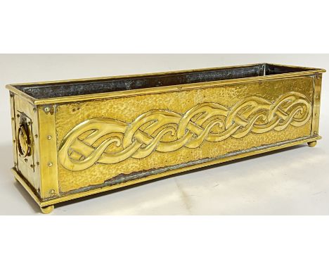 An Arts and Crafts/Art Nouveau repousse brass planter/trough with loop handles to side and planished finish, raised on four b