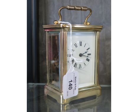 A brass carriage timepiece with white enamel dial and Roman numerals