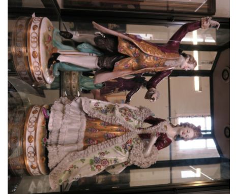 A pair of German porcelain figures dancing, wearing a purple coat and purple lace dress, the lady 40cm high 