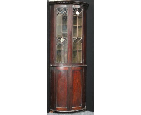 A 19th century mahogany floorstanding bow fronted corner display cabinet, dentil cornice above a pair of astragal glazed door