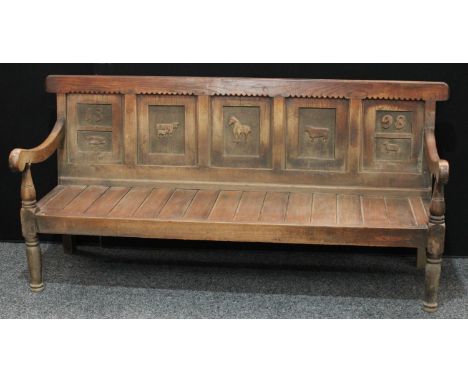 An 18th century oak settle, the five panelled back later carved in relief with animals and dated 1898, downswept open arms, p