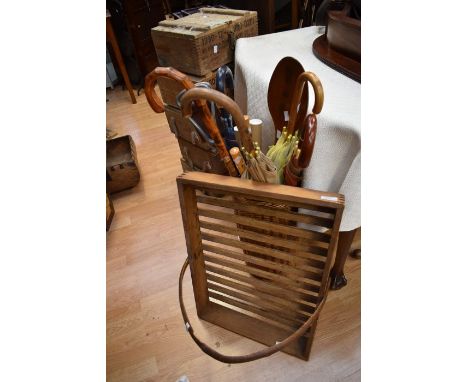 A wicker umbrella and stick stand with large novelty spoon umbrellas, truncheon along with a wooden vegetable rack