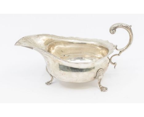 A Georgian style oval sauceboat, wavy rim, S-scroll handle on three shell and hoof feet, hallmarked by Haseler Brothers, Lond