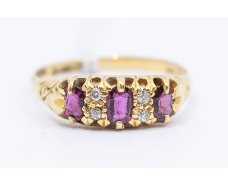 A George V three  stone ruby and diamond 18ct gold ring, comprising three oval cut rubies set to the front with diamond accen