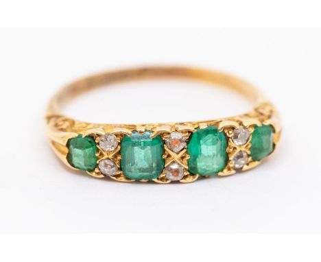 A early 20th century emerald and diamond 18ct gold ring, comprising five graduated emeralds with double diamond accents set b