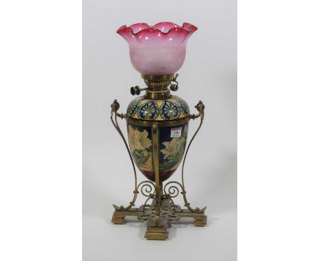 A Doulton Lambeth Faience oil lamp, decorated by Mary Butterton, circa 1870, having an associated cranberry tinted frilled gl