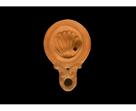 1st-2nd century AD. A terracotta oil lamp with volute scrolls to the nozzle, broad recessed discuss with low-relief scallop s