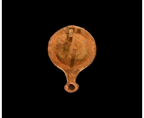 1st-3rd century AD. A hollow-formed iron lamp with broad discoid body, narrow neck and flared nozzle, central peg and coiled 