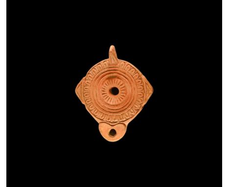 1st-2nd century AD. A terracotta oil lamp with discoid base, heart-shaped nozzle, lateral wings, flange handle to the rear; c