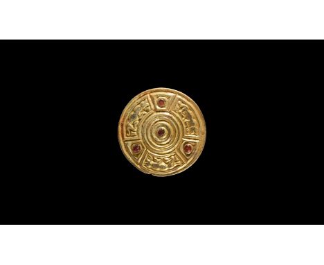 6th century AD. A silver-gilt disc brooch with segmented face, central garnet cabochon surrounded by concentric ring, three r