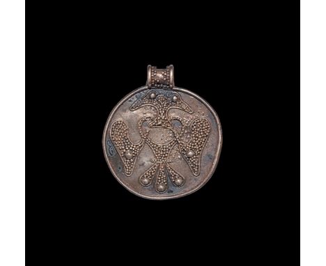 9th-12th century AD. A discoid silver pendant with raised rim, integral loop with granule detailing, applied granule and fili