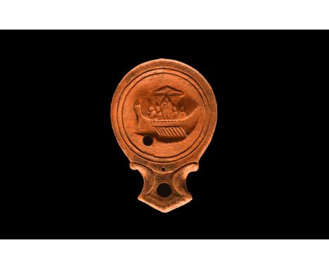 1st-2nd century AD. A squat terracotta oil lamp with volute scrolls to the nozzle, broad discus with profile galley and crew.