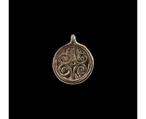 10th-11th century AD. A silver discoid pendant with pierced lug, low-relief motif with beaded border, reserved scrolls motif.