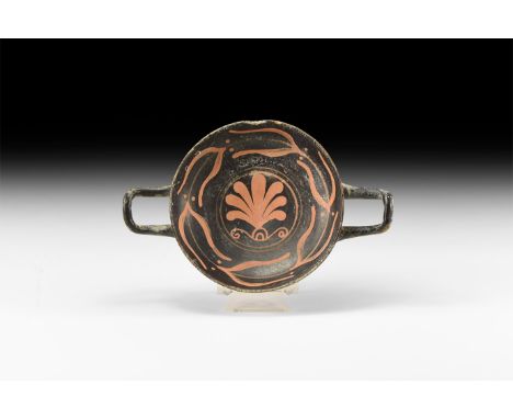 5th-3rd century BC. A ceramic blackware kylix with pedestal base and square handles, shallow bowl; band of laurel leaves and 