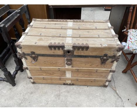 A 19TH CENTURY BANDED TRAVELLING TRUNK WITH EMBOSSED METAL DECORATIVE FITTINGS AND SMALL WHEELS 