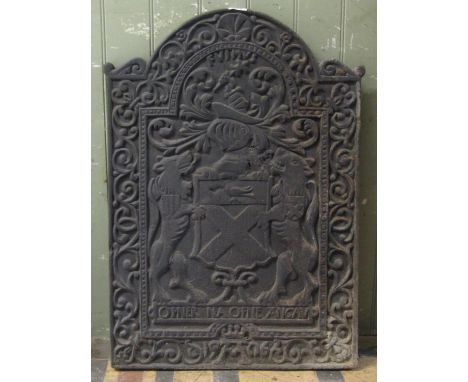 A cast iron fireback of stepped arched form, with raised relief armorial detail, Latin script and scrolling acanthus surround