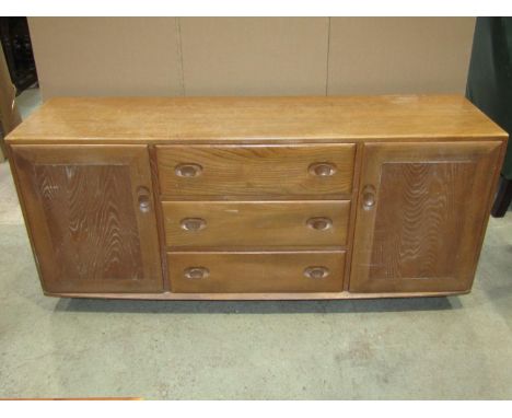 An Ercol Windsor elm low sideboard, fitted with three long central drawers flanked by cupboards with dished handles, raised o