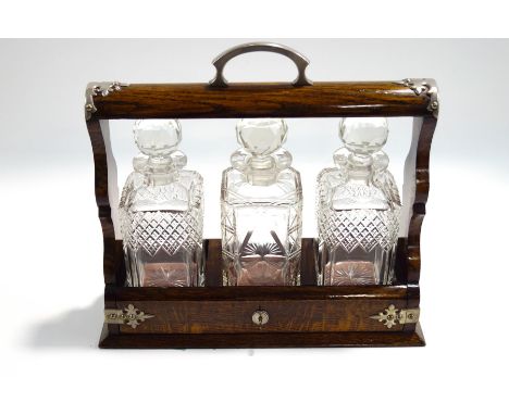 An early 20th century oak three decanter tantalus, with plated mounts